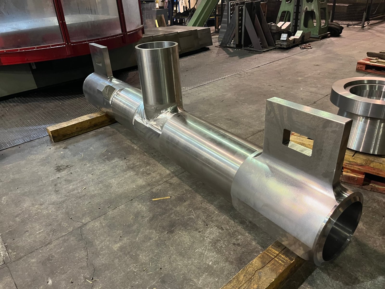 Long forged manifold assembly with a central branch and lifting brackets on the workshop floor